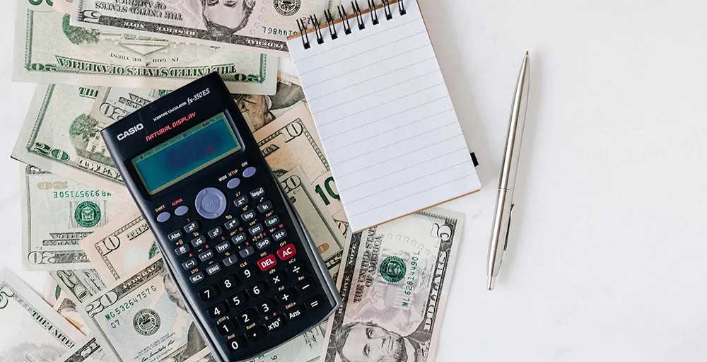 calculator and notepad placed over stack of paper bills