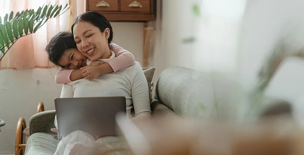 laughing little girl hugging mother with laptop