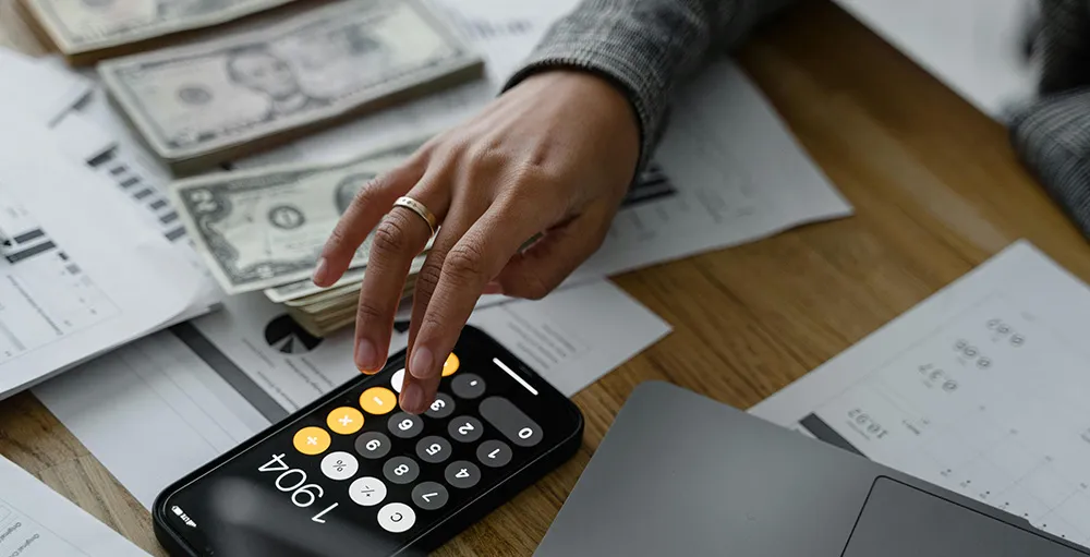 hand of a person using a calculator near cash money on wooden table