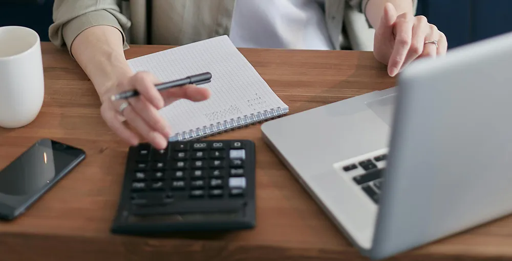 woman using a calculator while sitting in front of a laptop