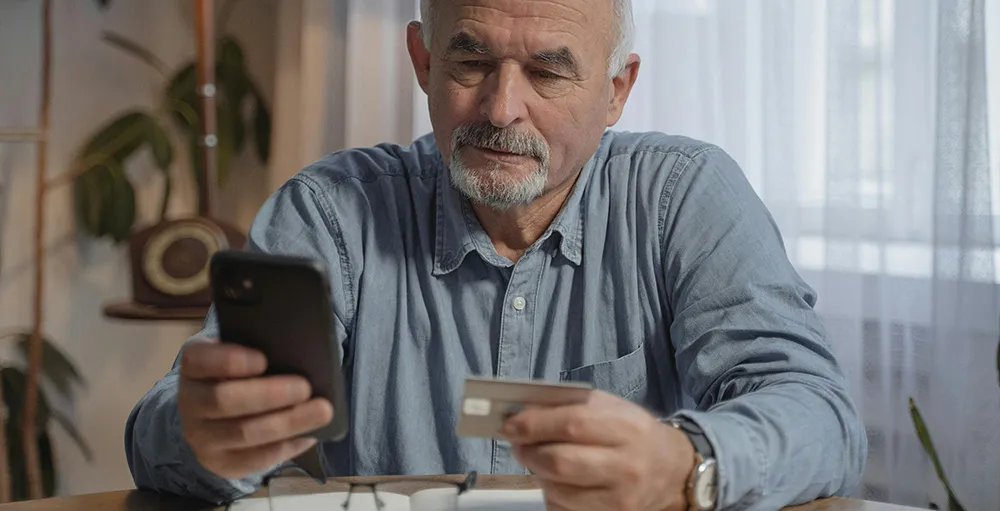 an elderly man holding his mobile phone and a credit card