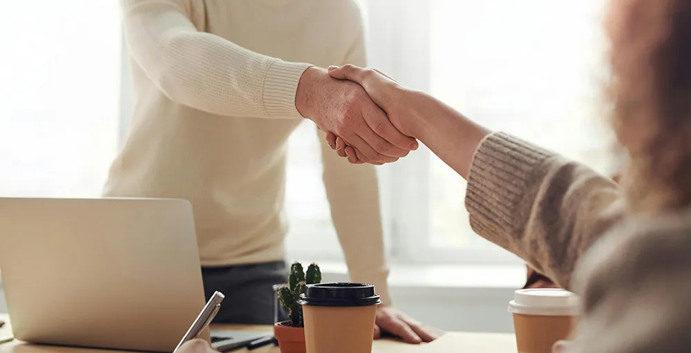 people shaking hands over desk during meeting