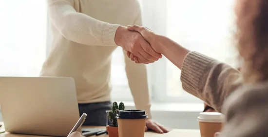 people shaking hands over desk during meeting
