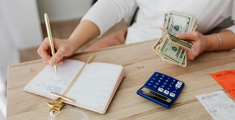 person writing in notebook while holding money