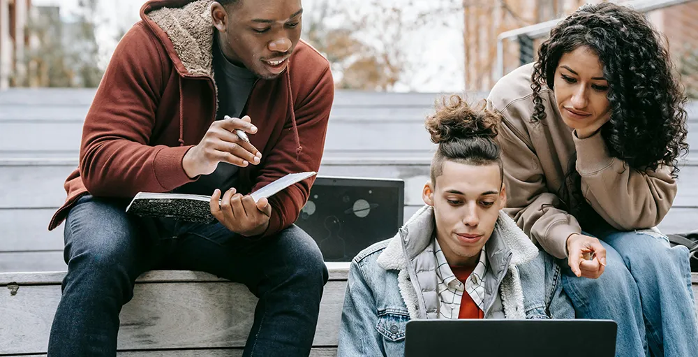 students studying on laptop with notebook on steps