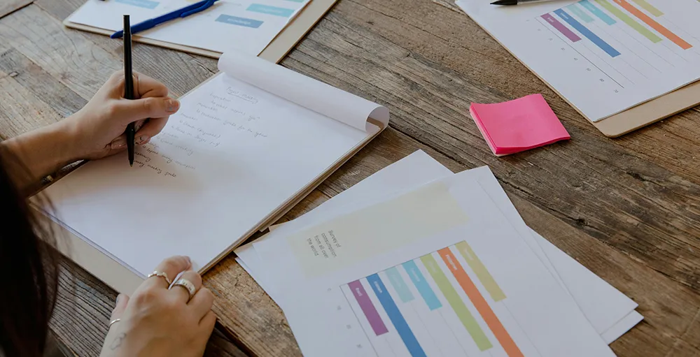 person writing on paper while reviewing spreadsheets