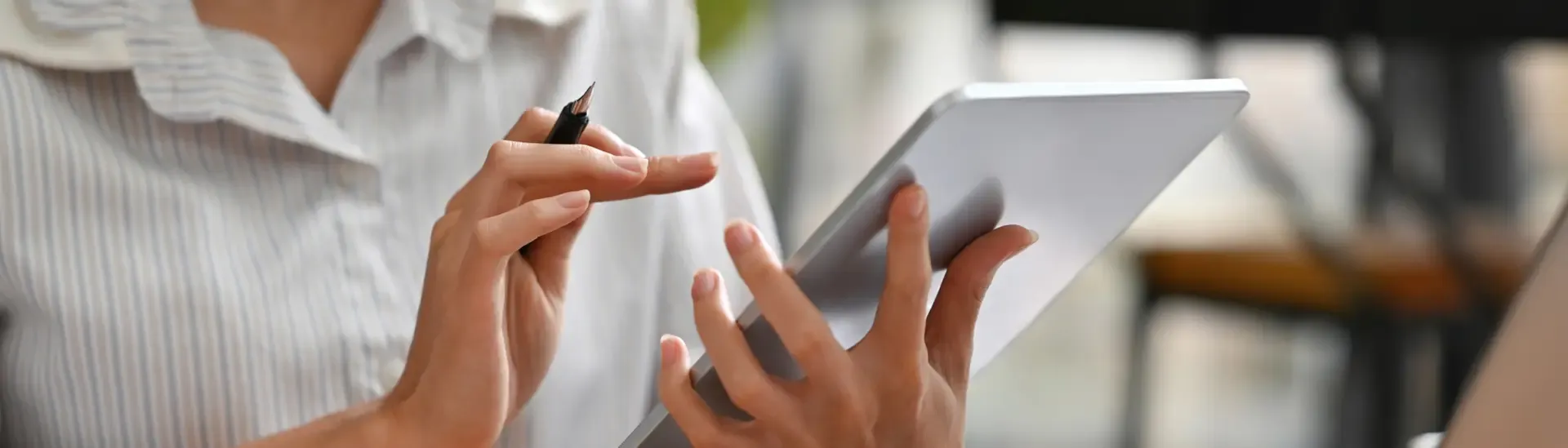 Person using a stylus on a tablet while wearing a striped shirt, with a blurred indoor background.