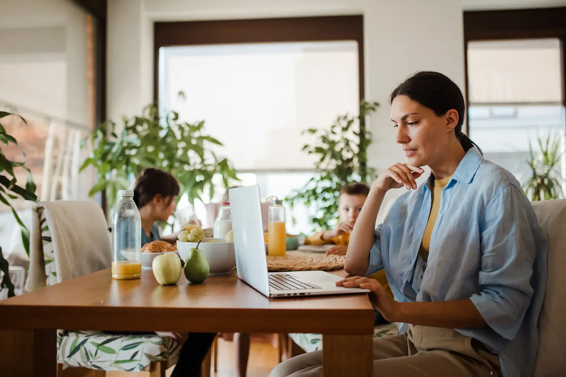 woman working on laptop at kitchen table while children have breakfast