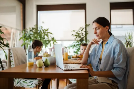 woman working on laptop at kitchen table while children have breakfast