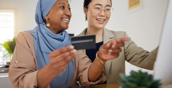 smiling women are seated at a desk in front of a computer