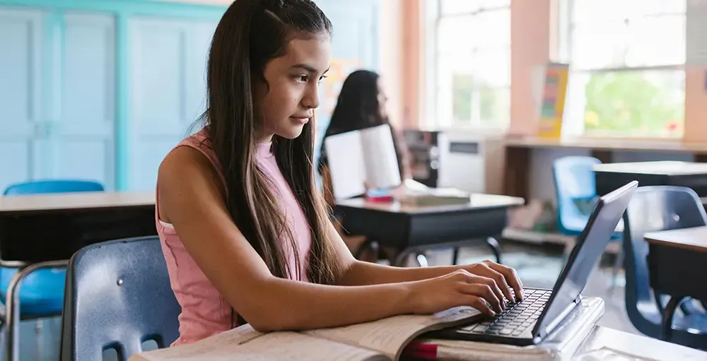 young girl working on laptop in school