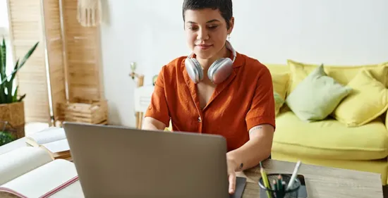young woman with short dark hair is working on a laptop at a desk in her home